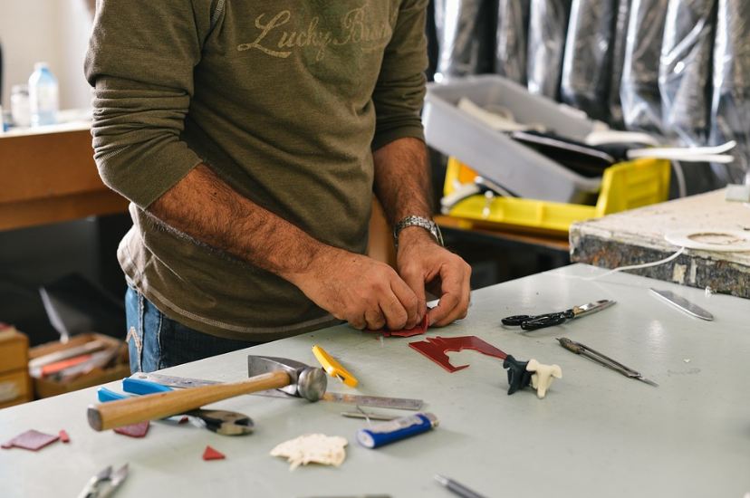 hands of a man working, a hammer, a man wearing green, scissors, various things on the table