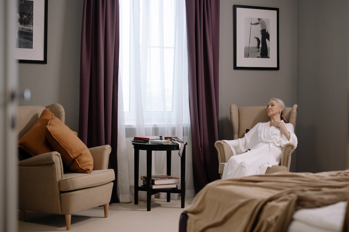 elderly woman in sitting on sofa chair inside a bedroom