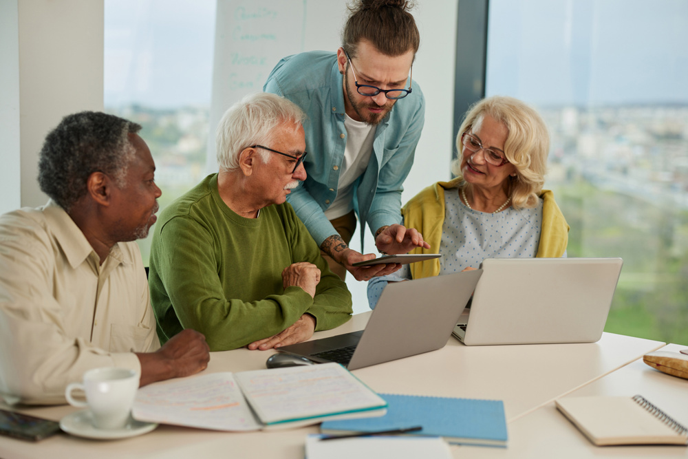 Multicultural group of senior students asking questions their tutor who showing them solution