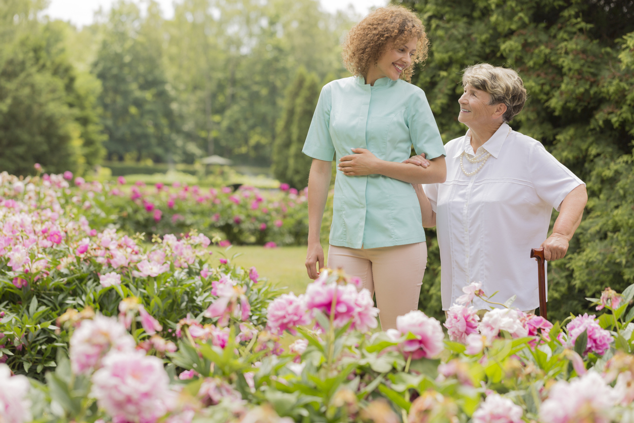 a happy elderly woman walking with her nurse around the garden